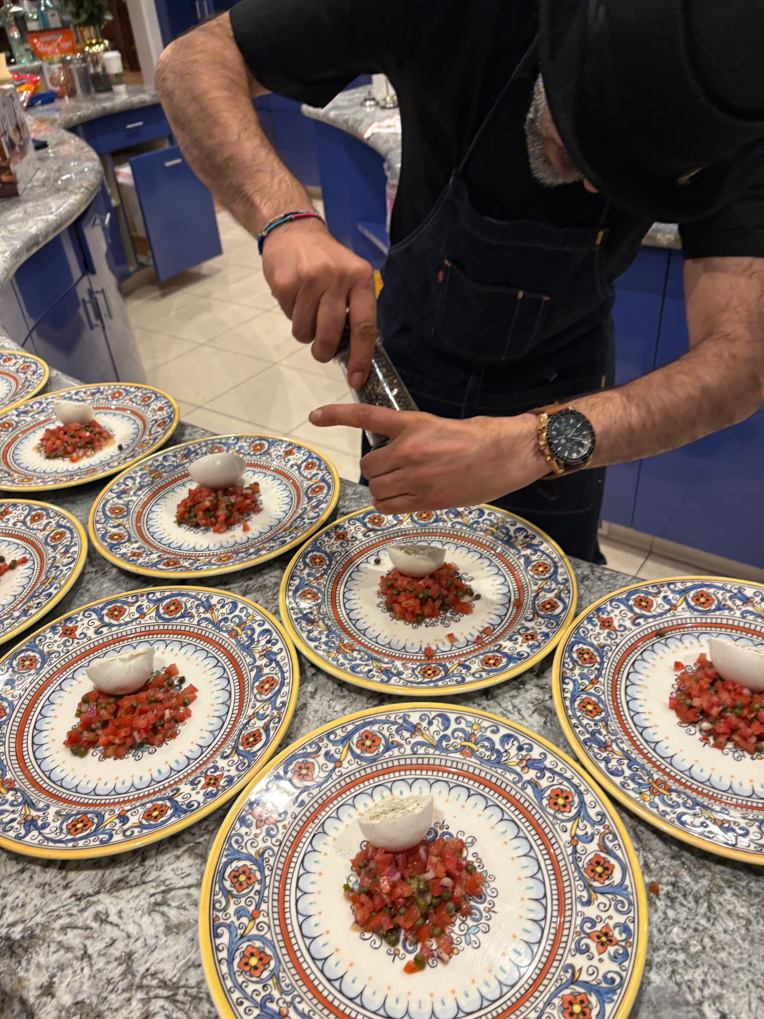 A chef adds freshly ground pepper to creamy cheese and tomato plates