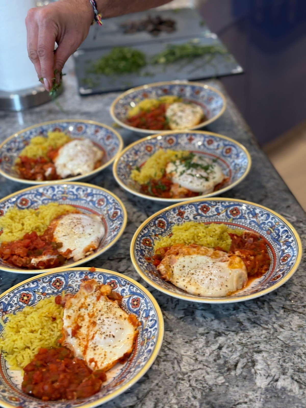 A chef garnishes plated eggs with yellow rice and vegetables